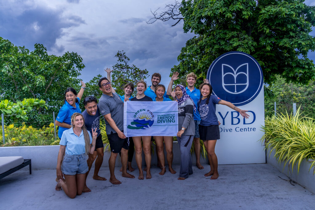 The smiling YBD Dive Centre crew proudly holding their Green Fins Gold award certificate for the year 2026 at the dive centre